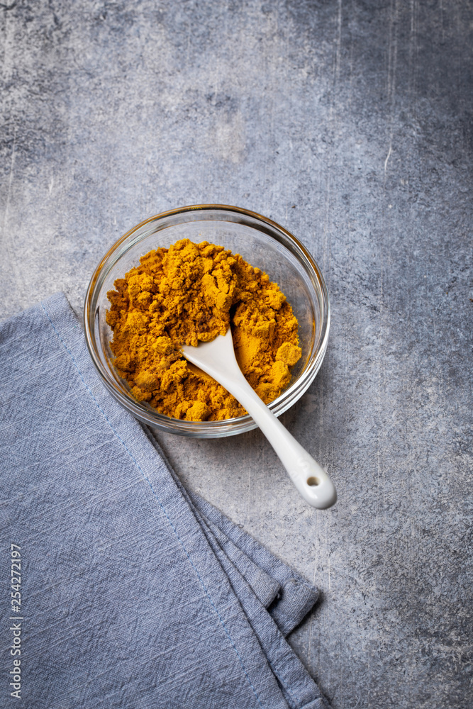 Fototapeta premium Turmeric powder in glass bowl with spoon on gray grunge background