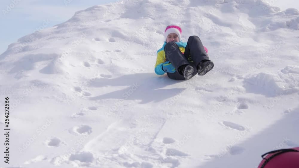 Happy little girl climbs the hill and sliding in the snow. Beautiful sunny day, the child is having fun playing with snow.