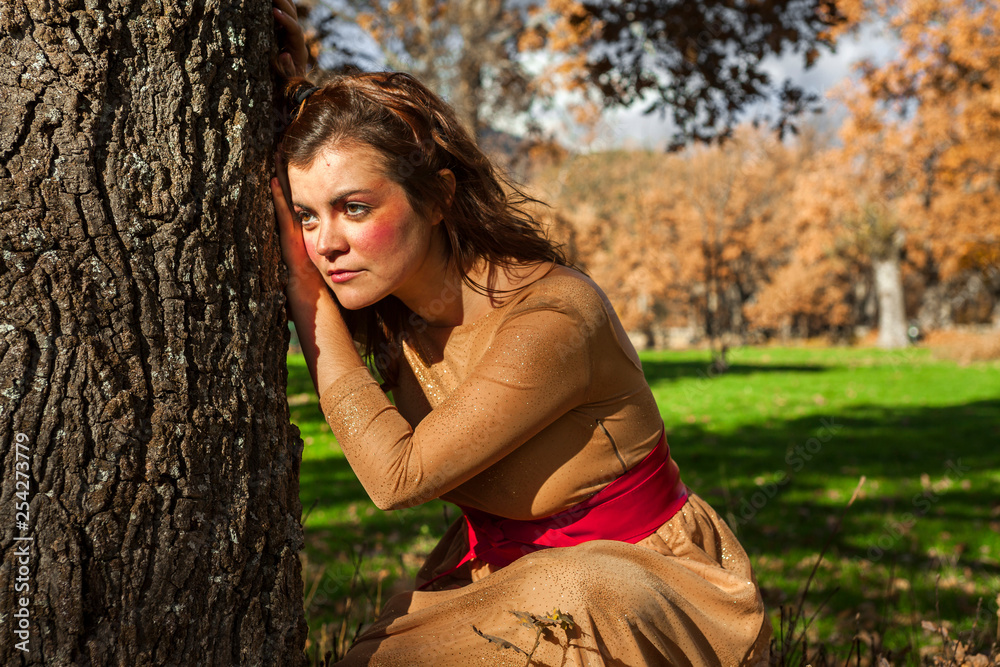 Medium shot portrait elegant young woman standing in a tree. Looking out. Sunset autumn Medium shot portrait elegant young woman standing in a tree. Looking out. Sunset autumn