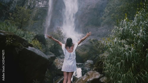 Back view happy young tourist woman with arms wide open enjoying moments of freedom at epic Sri Lanka jungle waterfall. photo