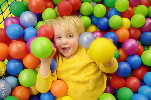 Happy little boy having fun in ball pit with colorful balls. Child playing on indoor playground. © Maria Sbytova