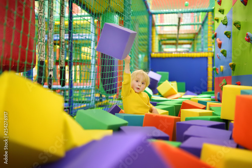 Cute little boy plays with soft cubes in the dry pool in play center. Kid playing on indoor playground in foam rubber pit in trampoline.