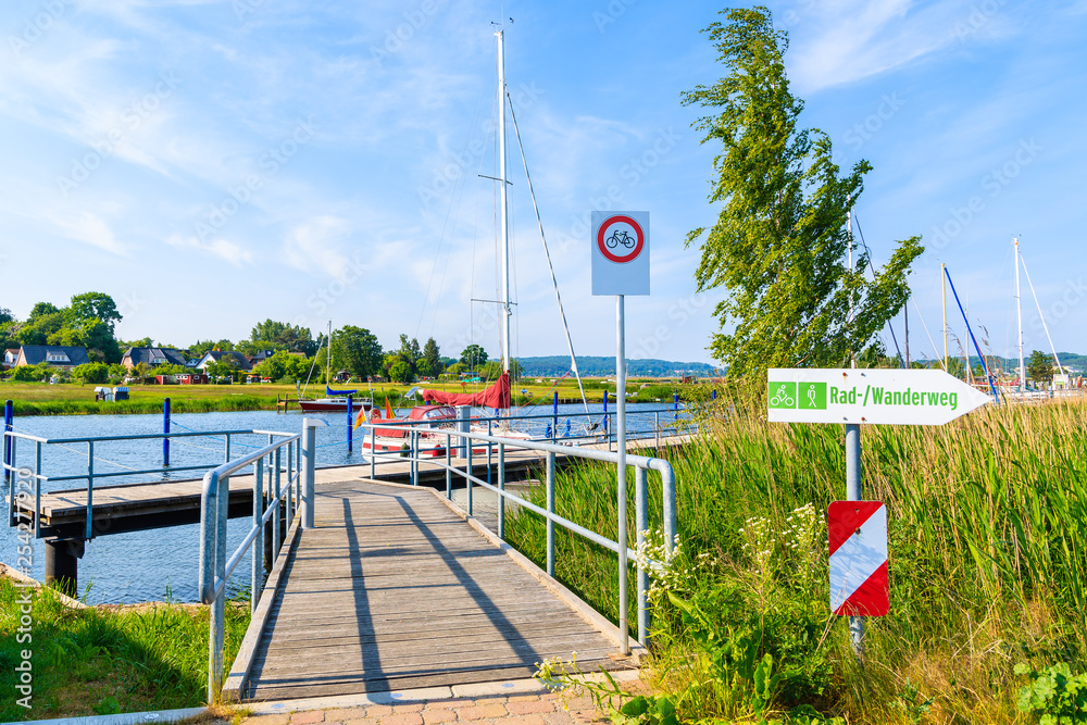 Walkway to pier with sailing boats anchoring on beautiful lake in Moritzdorf village on coast of Rugen island, Baltic Sea, Germany Walkway to pier with sailing boats anchoring on beautiful lake in Moritzdorf village on coast of Rugen island, Baltic Sea, Germany