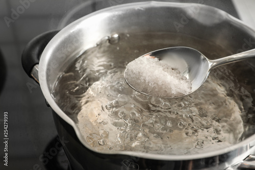 Salting boiling water in pot on stove, closeup