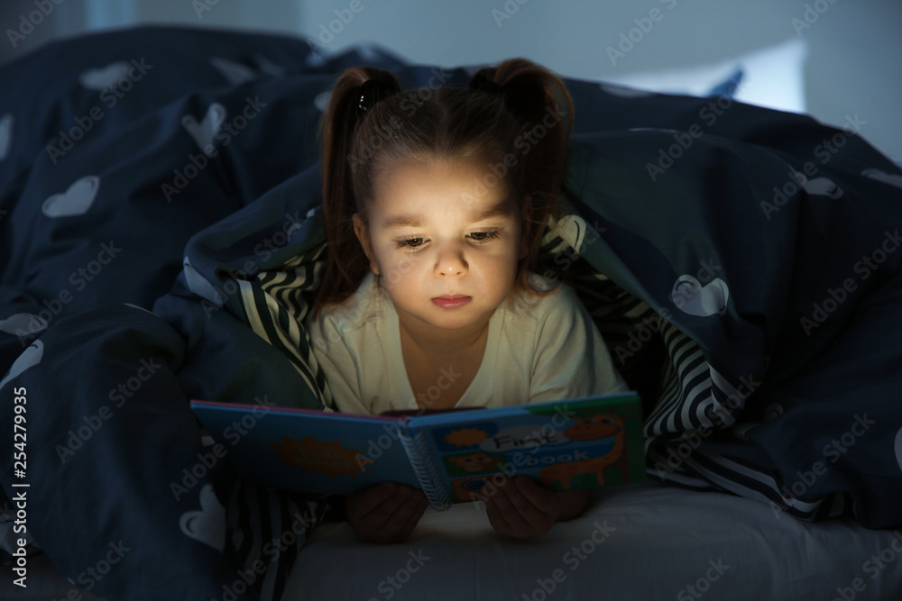 Beautiful little girl reading book in bed at night. Bedtime story Beautiful little girl reading book in bed at night. Bedtime story