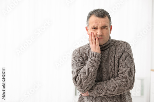 Mature man suffering from strong tooth pain on light background, space for text