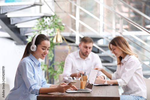 Young businesswoman with headphones  laptop and her colleagues at table in office