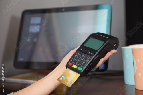 Woman using credit card machine for non cash payment in cafe, closeup. Space for text photo