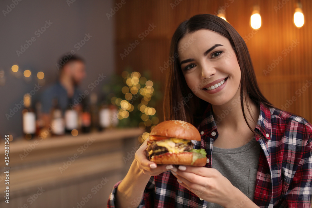 Young woman eating tasty burger in cafe