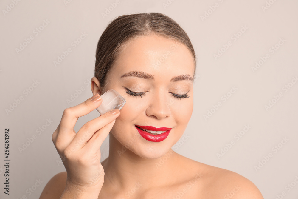 Young woman with ice cube on light background. Skin care