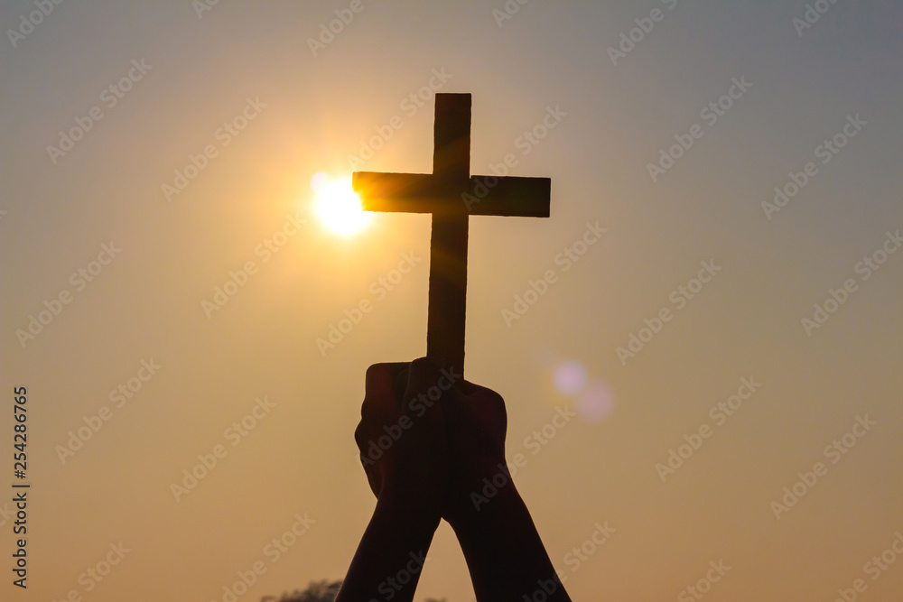 human hands praying to the GOD while holding a crucifix symbol with bright sunbeam on the sky human hands praying to the GOD while holding a crucifix symbol with bright sunbeam on the sky
