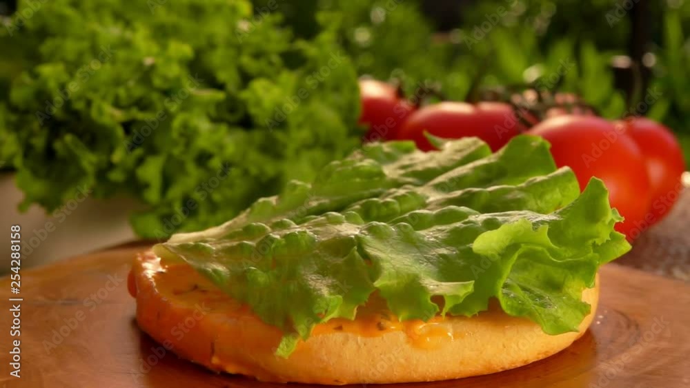 Leaf of lettuce falls onto a hamburger bun with sauce Leaf of lettuce falls onto a hamburger bun with sauce