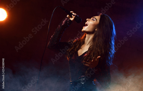 Beautiful singing girl curly afro hair. Beauty woman singer sing with microphone karaoke song on stage smoke, spotlights photo