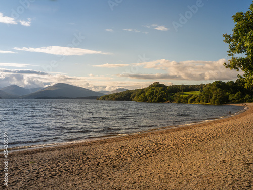 beach at a lake (loch lomond) on a sunny day with mountains in the background