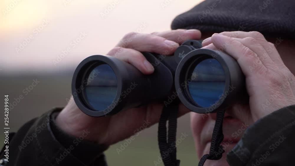 Private detective spying on someone with long binoculars outdoors, close up shot