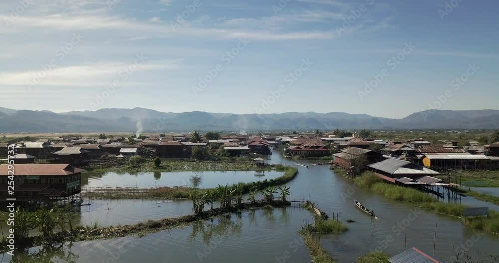 Shan State, Myanmar. Aerial view of a traditional long tail boat approaching a village on Inle Lake. Mountains view in the background. Shan State, Myanmar. Aerial view of a traditional long tail boat approaching a village on Inle Lake. Mountains view in the background.