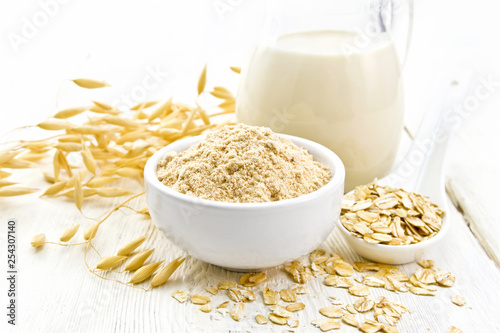 Flour oat in bowl with milk on light wooden board