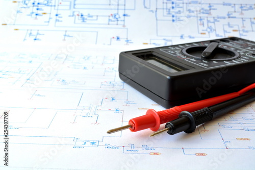 measuring device electric tester with red and black probe on background of large sheet of paper with drawn color electrical circuit