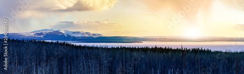Panoramic frozen winter landscape view of Yellowstone National Park with sunlight shining in the background of the snowy mountain range