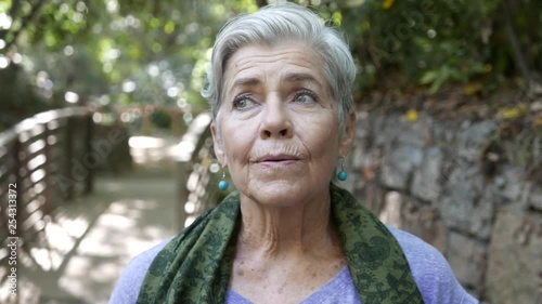 Pretty older woman takes a deep breath and looks around her surroundings at park
