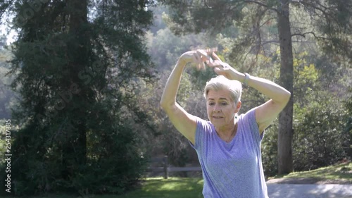 Senior citizen woman stretches and practices yoga in the park.