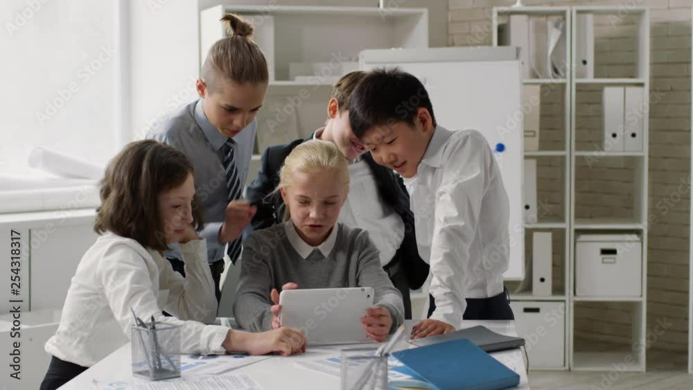 Wide shot of kids surrounded blonde Caucasian girl with tablet in her hands