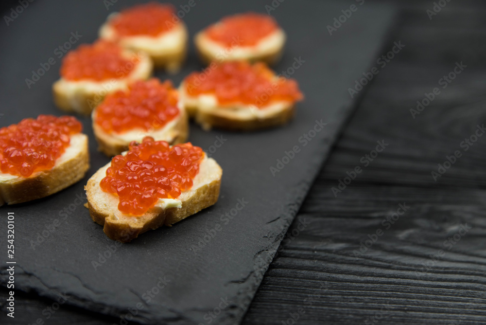 Sandwich from white baguette bread with red salmon caviar on black plate. Russian seafood cuisine. Concept of wealth and riches. Sandwich from white baguette bread with red salmon caviar on black plate. Russian seafood cuisine. Concept of wealth and riches.