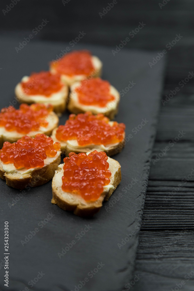 Sandwich from white baguette bread with red salmon caviar on black plate. Russian seafood cuisine. Concept of wealth and riches. 