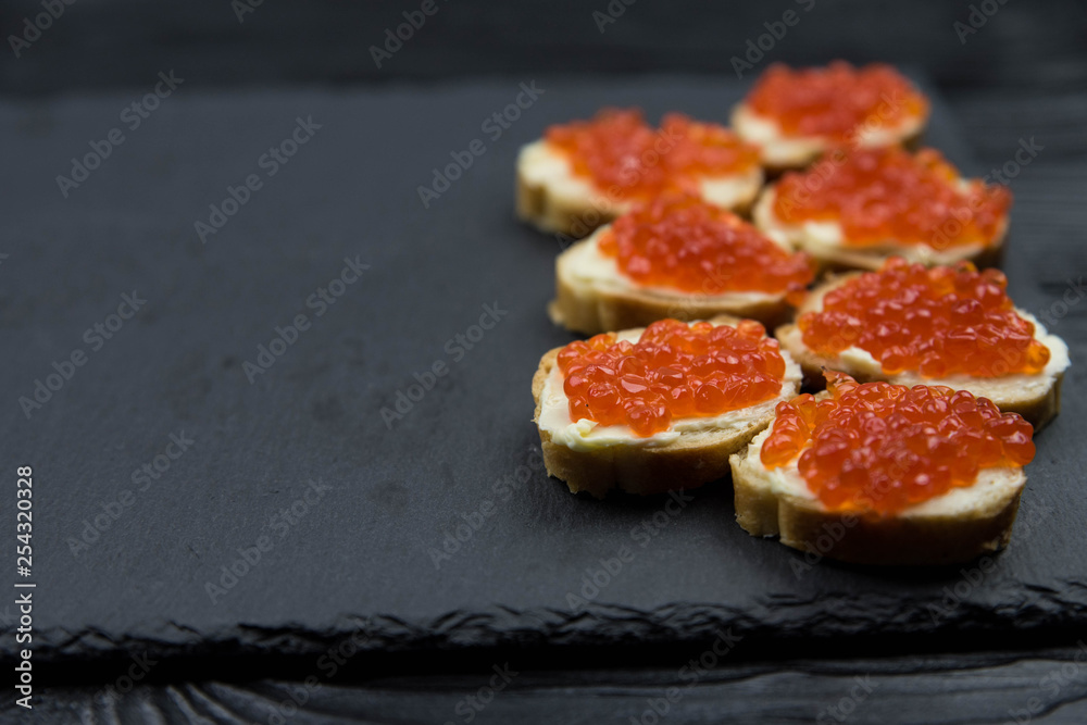 Sandwich from white baguette bread with red salmon caviar on black plate. Russian seafood cuisine. Concept of wealth and riches. 