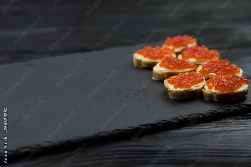 Sandwich from white baguette bread with red salmon caviar on black plate. Russian seafood cuisine. Concept of wealth and riches. 