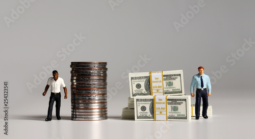 A pile of bills and coins. Miniature people. The concept of racial and income disparity.