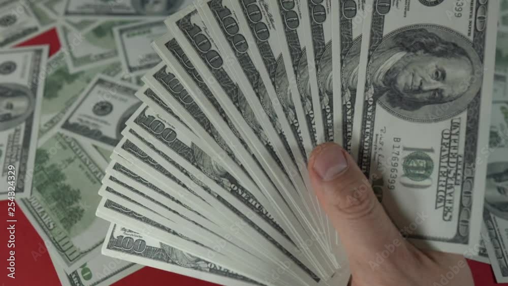 Locked shot of a male Hand wagging around with a stack of hundred of US Dollars in front of a red table full of money. Locked shot of a male Hand wagging around with a stack of hundred of US Dollars in front of a red table full of money.