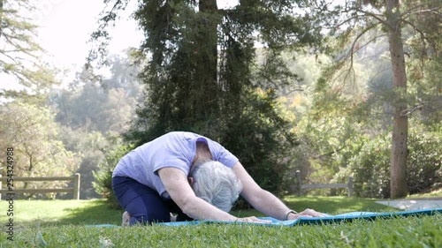 Senior citizen woman stretches and does yoga in the park on a sunny day.