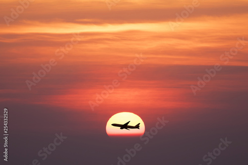 Beautiful sunset with silhoette air plane is flying through the sun. © BUSARA