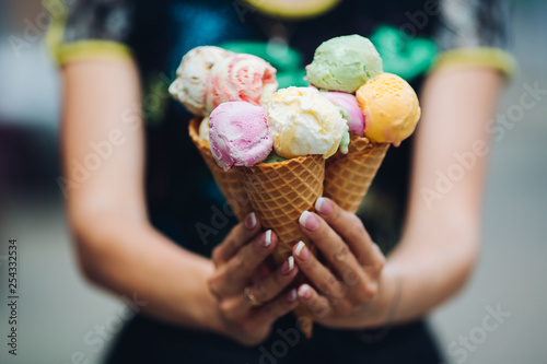 Crop of woman's hand holding delicious colorful ice cream, looking tasty, sweet, mouthwatering, perfect for summer heat while sunny day. Pretty nails with professional french manicure. Food concept.