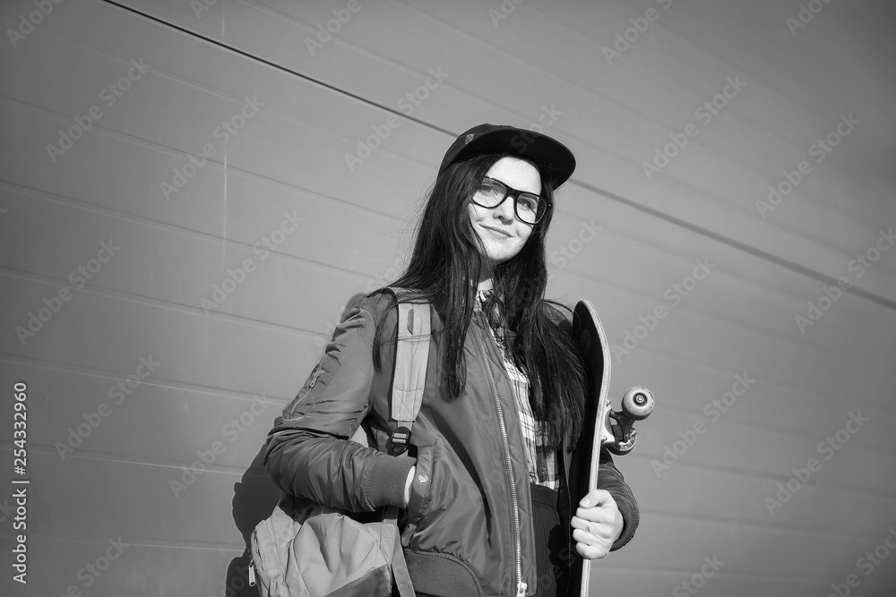 Naklejka premium A young hipster girl is riding a skateboard. Girls girlfriends for a walk in the city with a skateboard. Spring sports on the street with a skateboard.