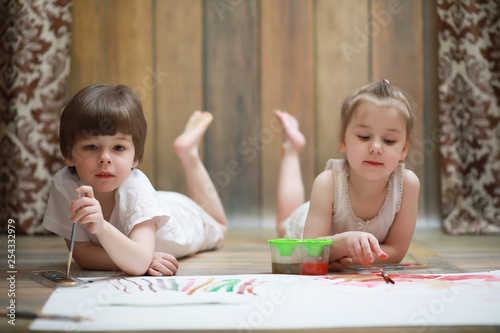 Little children paint on a large sheet of paper