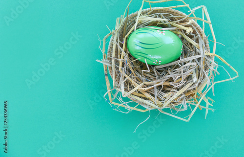 Easter eggs in basket nest decoration on green background - top view