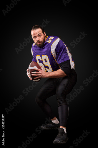 Portrait of American football player throwing ball over black background