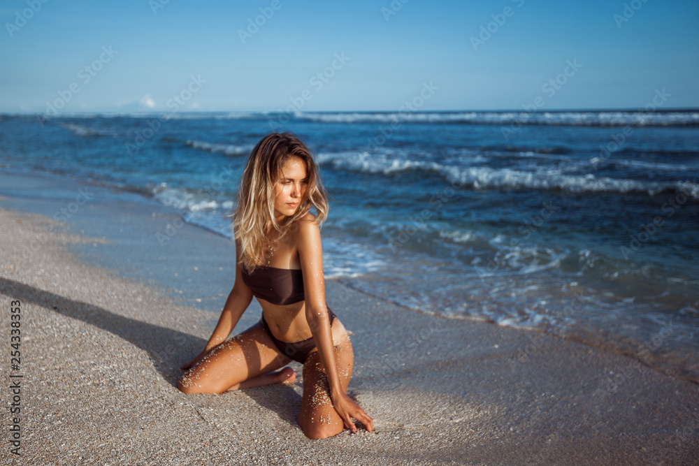 Sexy girl in brown swimsuit sits on her knees bent over the beach in the sand Sexy girl in brown swimsuit sits on her knees bent over the beach in the sand