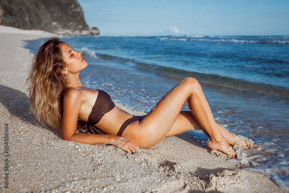 Skinny tanned girl in a swimsuit lying on the beach