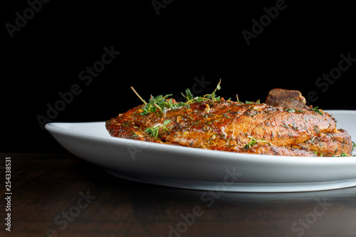 Roast pork knuckle on white plate, sprinkled with rosemary.