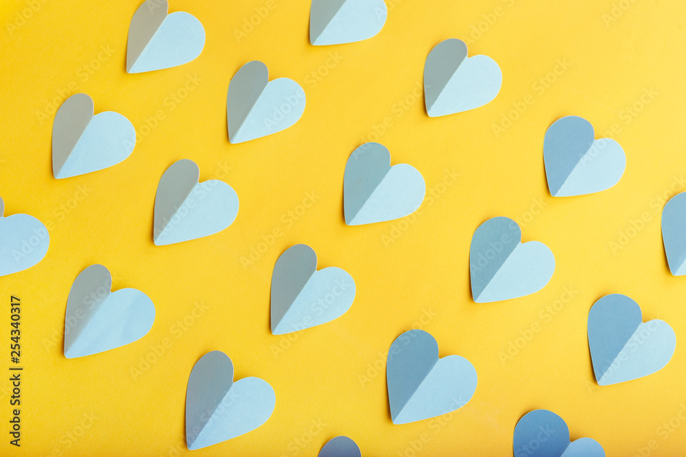 Flat lay of blue paper hearts in rows on yellow background