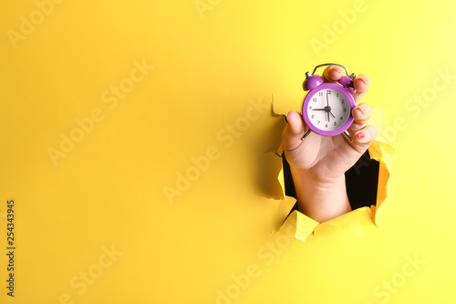 Female hand with alarm clock visible through hole in torn color paper photo
