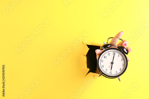 Female hand with alarm clock visible through hole in torn color paper photo