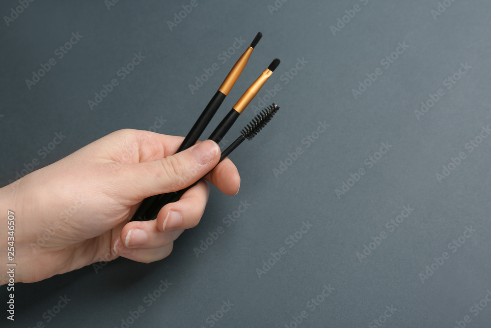 Female hand with tools for eyebrows correction on grey background Female hand with tools for eyebrows correction on grey background