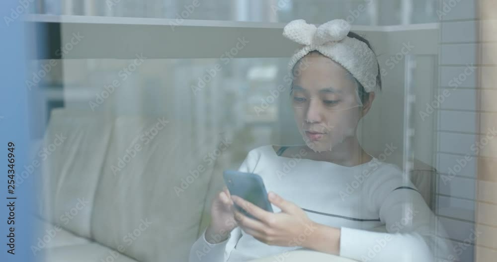 Woman apply paper mask and use of mobile phone at home with window reflection Woman apply paper mask and use of mobile phone at home with window reflection