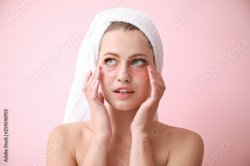 Young woman with under-eye patches on color background