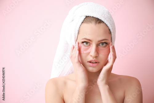 Young woman with under-eye patches on color background