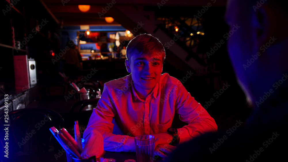 A man in shirt sitting in the bar with neon lighting by the table